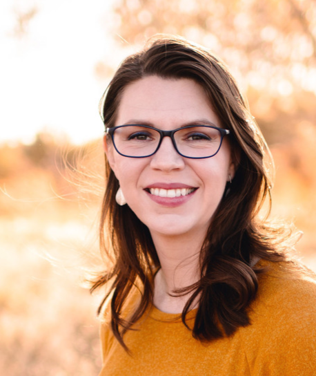 Headshot photo of author C.W. Allen, a middle aged white woman with shoulder-length straight brown hair. She is wearing blue eyeglasses and a mustard yellow shirt, standing outdoors against a gold-colored autumn background